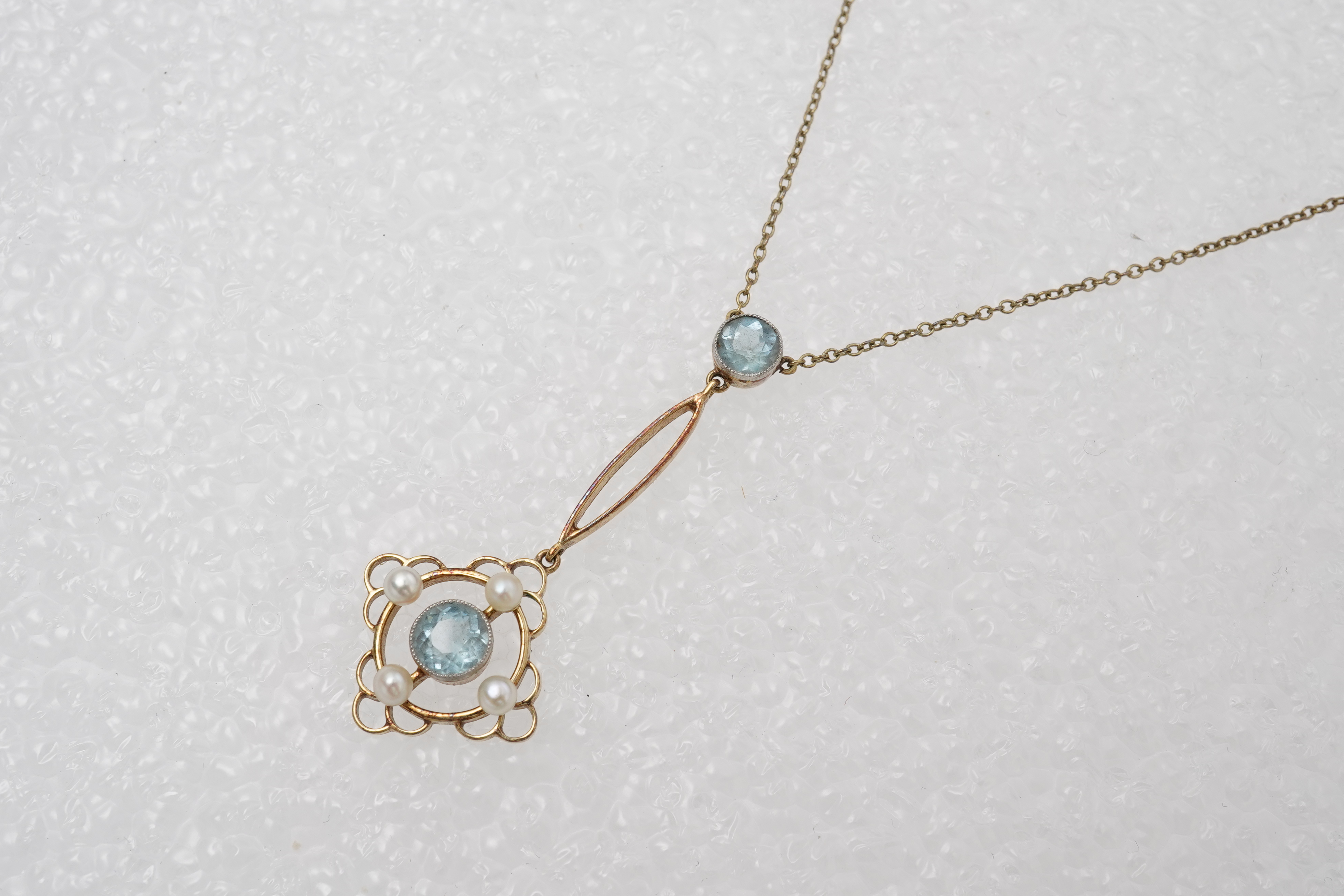 An Edwardian circular-cut aquamarine and seed pearl pendant, early 20th century, of foliate design, mounted in gold, pendant length 4cm, chain length 40cm, clasp stamped 15, gross weight approximately 3 grams, pearls unt